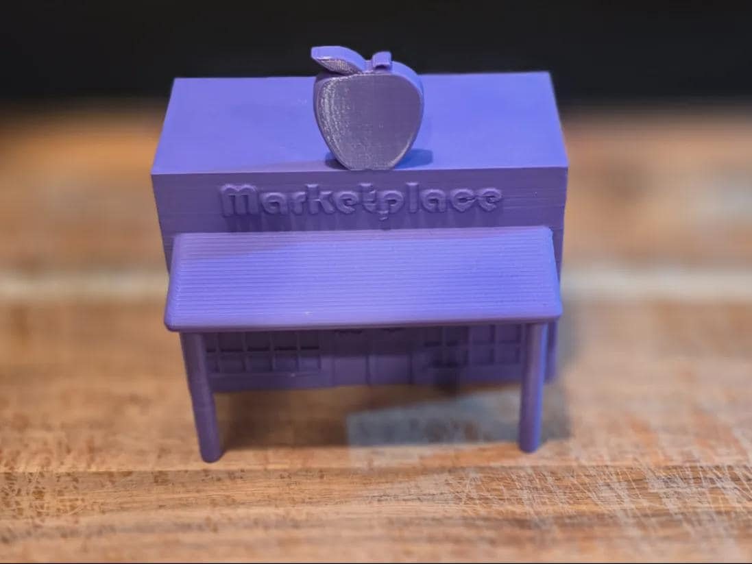 Purple 3D-printed miniature market facade with an awning and apple sign