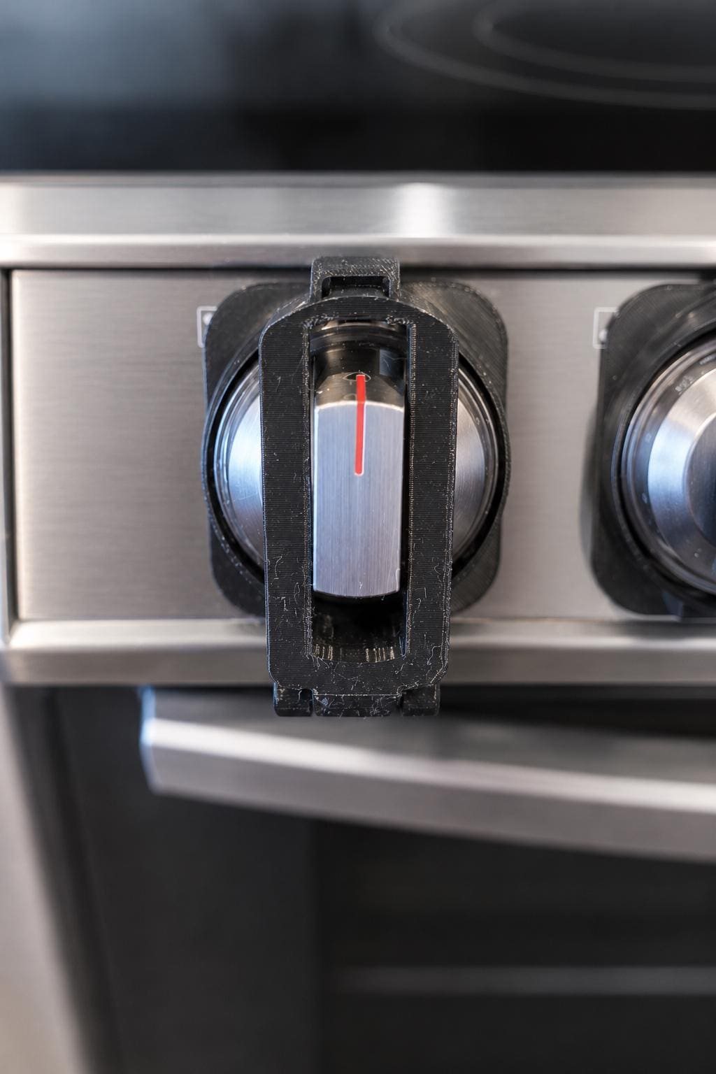 Black 3D-printed guard installed around a stainless-steel stove knob